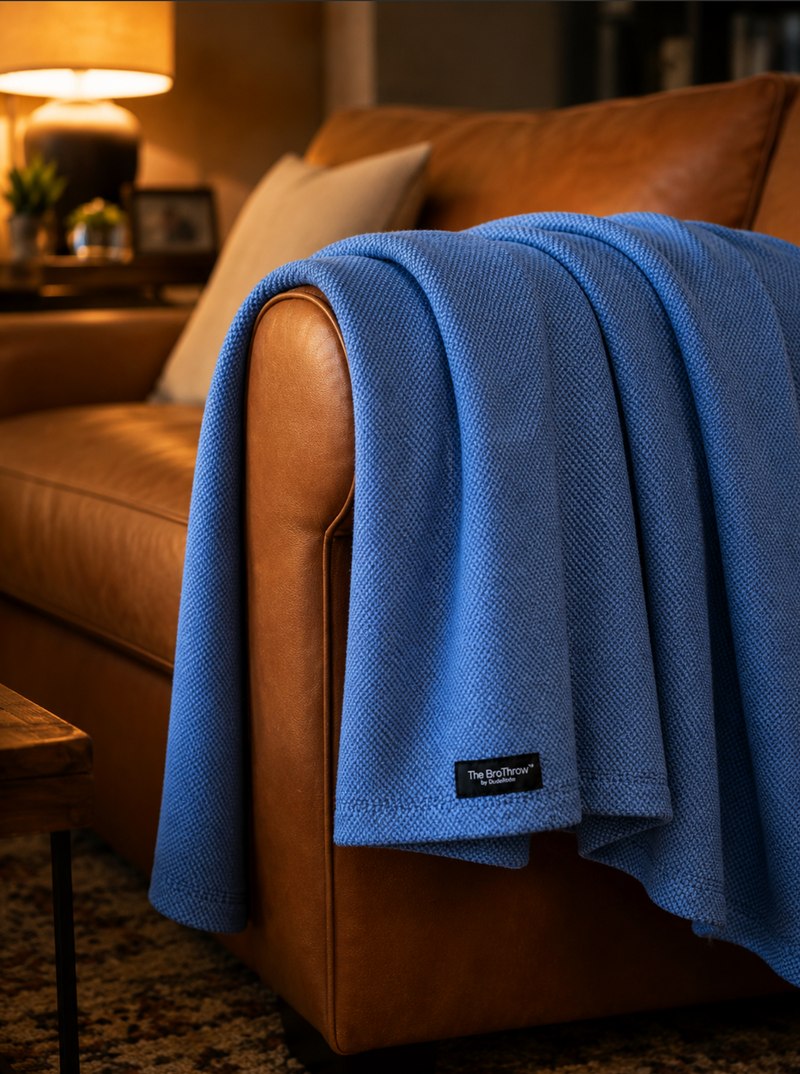 Blue blanket draped over a brown leather sofa in a cozy living room.