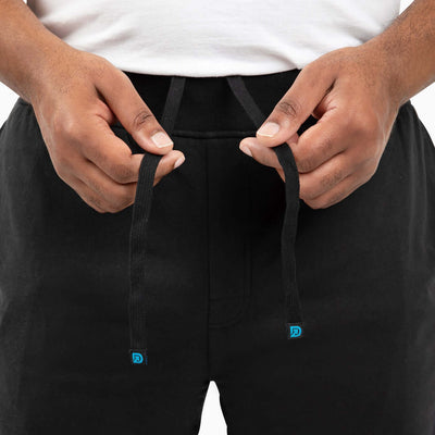 Close-up of hands adjusting drawstrings on black men's shorts for versatile wear.