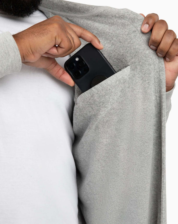 Man placing smartphone in pocket of a grey DudeRobe, showcasing modern design and functional style.