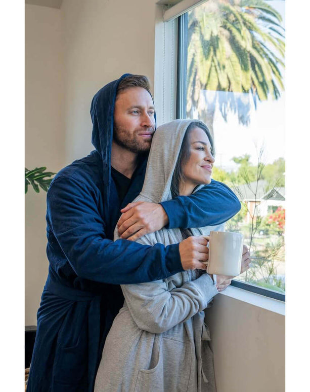 Couple enjoying cozy moments in DudeRobe luxury hooded bathrobes by the window, perfect for relaxation.