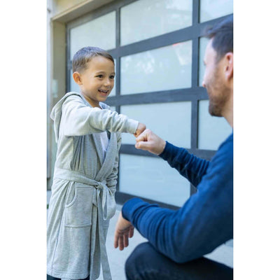 A happy boy wearing the UFC DudeRobe sharing a fist bump with an adult in a modern setting.