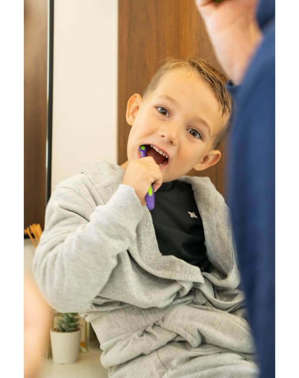 Smiling boy in a stylish luxury hooded bathrobe brushing his teeth in a modern bathroom.