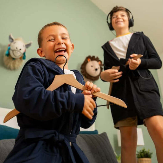 Two kids enjoying their time in a Luxury Kids Hooded Bathrobe, one holding a hanger, displaying fun and comfort.
