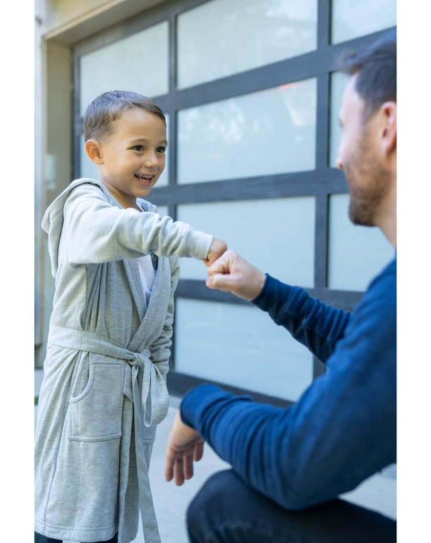 Smiling boy in a luxury kids hooded bathrobe giving a fist bump to an adult, showcasing fun family moments.
