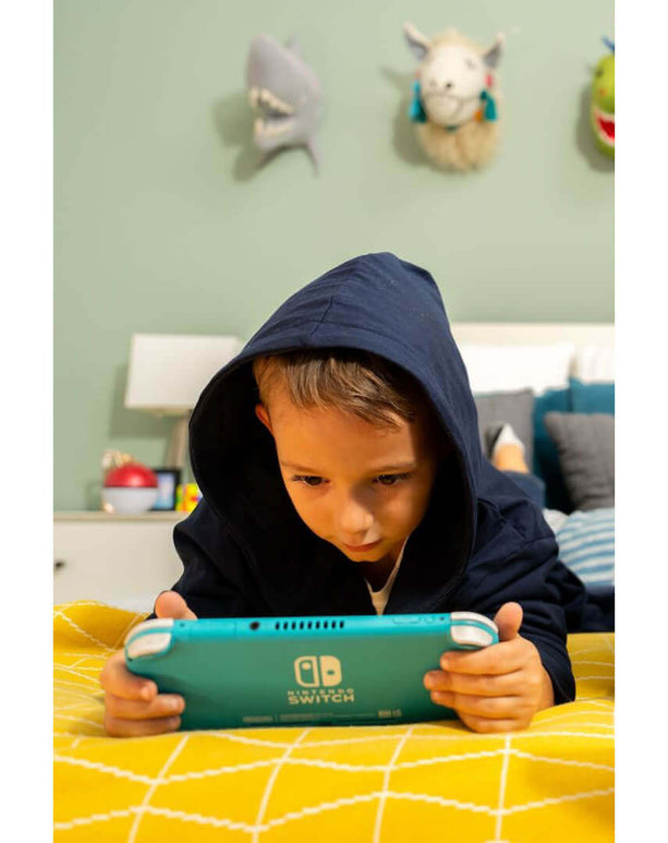 Kid in a luxury hooded bathrobe playing Nintendo Switch on a cozy yellow blanket.