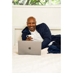 Man relaxing in a navy UFC DudeRobe while enjoying a drink and using a laptop for fight night. UFC merch.