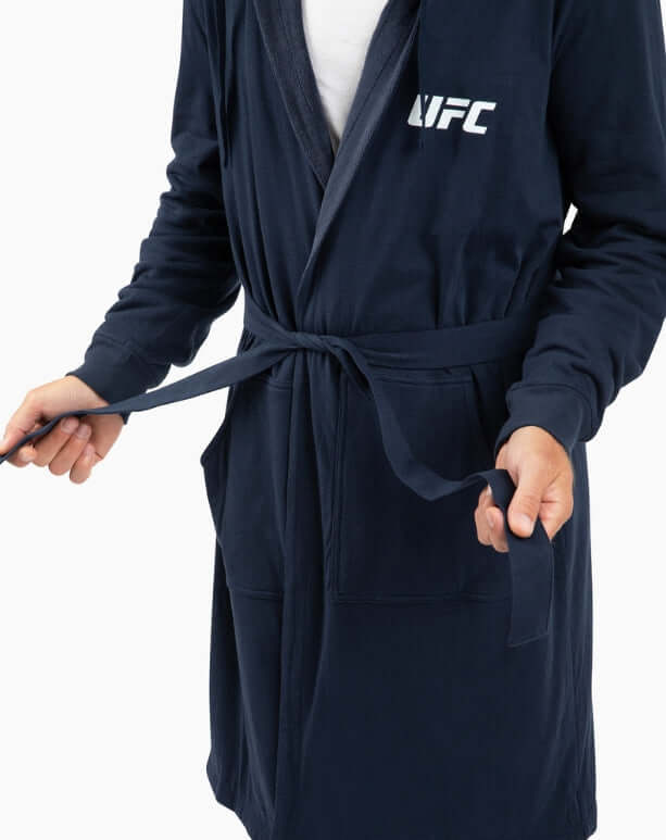 Man tying the belt of a navy UFC DudeRobe, a stylish modern bathrobe for lounging and relaxation.
