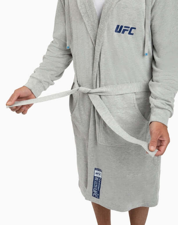Man wearing a grey UFC DudeRobe, tying the belt, featuring modern design and comfort for lounging.